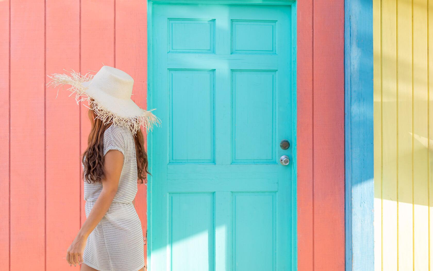 woman in a straw hat walking past brightly colored walls and door