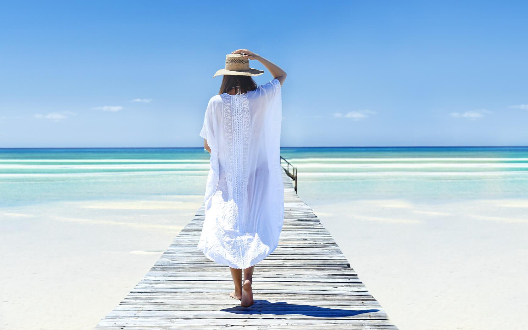 woman in straw hat and sundress walking on beach boardwalk