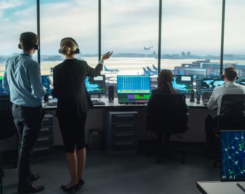 man in airport looking out window at plane taking off