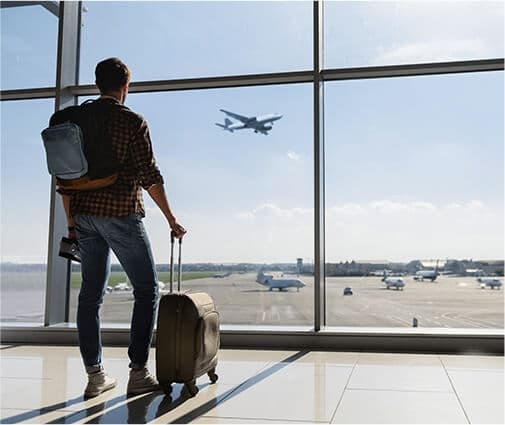 man in airport looking out window at plane taking off